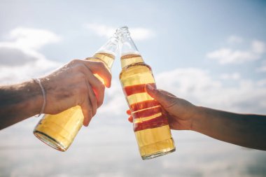 Güneş ışığında elinde bira olan iki şişeyi gökyüzüne yaklaştır.