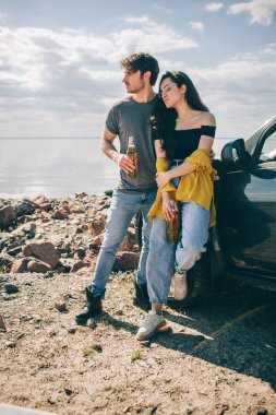 Seyahat, turizm, deniz kenarında piknik. Macera yaşayan bir çift. Araba yolculuğu konsepti. Erkek ve kadın bira içerler.
