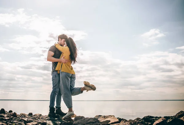 Szerelem és utazás. Egy pár az öböl hátterében áll. Egy férfi és egy nő áll egy folyó vagy tenger mellett köveken és ölelkeznek.. — Stock Fotó