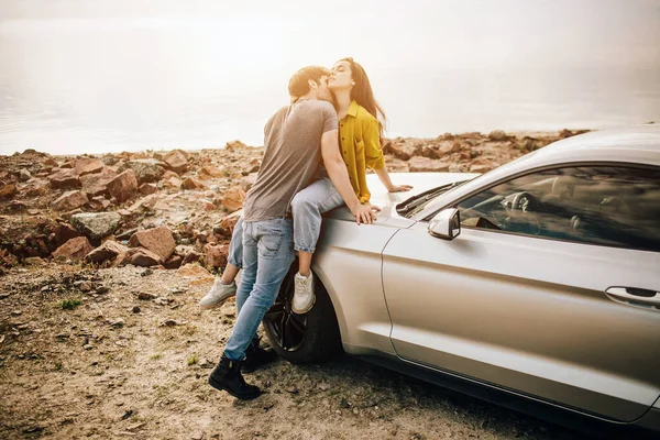 Casal jovem romântico compartilhando um momento especial ao ar livre. Casal jovem apaixonado em uma viagem de carro. Casal abraçando uns aos outros enquanto sentado no capô de seu carro na natureza . — Fotografia de Stock