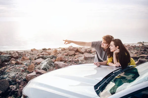 Pareja joven junto a un coche deportivo aparcado en la playa. Romance y amor en un viaje en coche — Foto de Stock