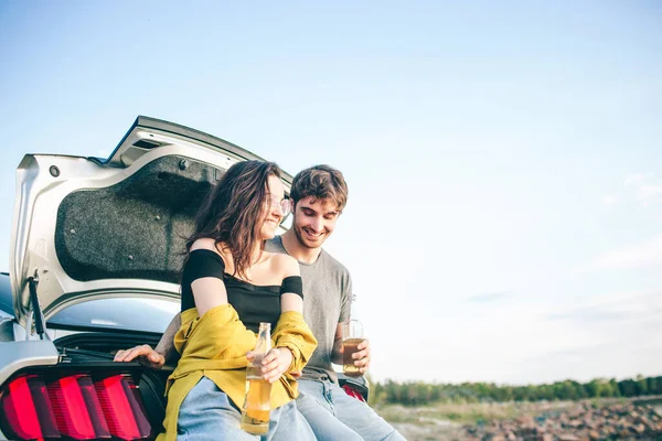 Viajes, turismo - Hombre y mujer beber champán cerca del agua en una mesa plegable portátil. Picnic cerca del agua. Un par de aventuras. Concepto de viaje . — Foto de Stock