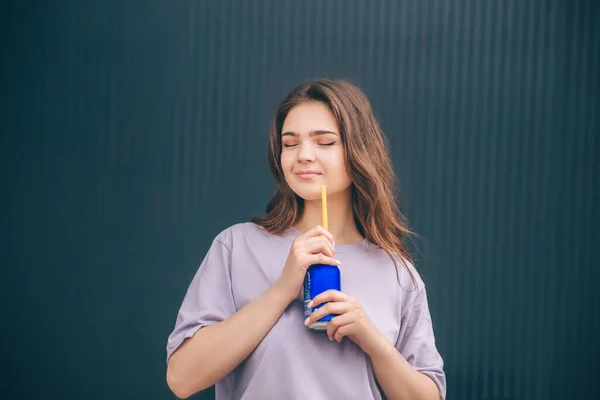 Jeune femme tendance et élégante isolée sur fond bleu gris. Fille profiter de son temps seul au mur sombre boire soda. Femme élégante en chemise violette. — Photo