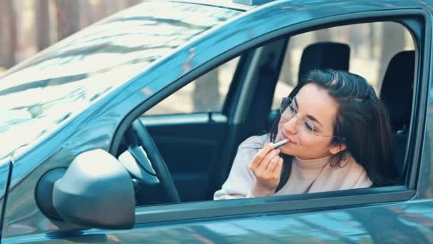 Mujer joven sentada en coche durante la pausa de viaje. La cámara lenta de la muchacha que aplica el lápiz labial en los labios. Tiempo de cosméticos y cuidado facial. Maquillaje de rutina . — Vídeos de Stock
