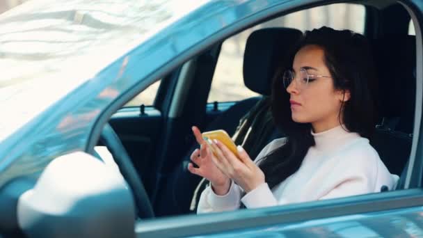 Mladá žena sedí v autě během cestovní přestávky. Šťastná veselá holka někomu volá a mluví na žlutém smartphonu. Komunikace v autě a konverzace. Veselá žena mluví. — Stock video
