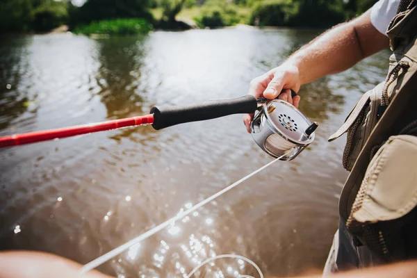 Νεαρός ψαράς που ψαρεύει στη λίμνη ή στο ποτάμι. Κόψτε την άποψη του ράβδου στα χέρια των ανδρών. Επαγγελματικό χόμπι του ποταμού. Πιάνω ψάρια με καλάμι. Κόψτε θέα. Ηλιόλουστη μέρα. — Φωτογραφία Αρχείου