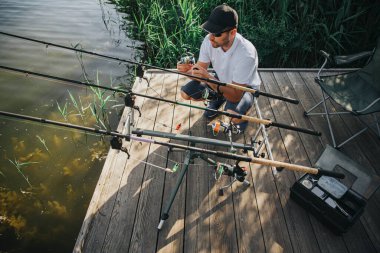 Gölde ya da nehirde balık tutan genç bir balıkçı. Balıkçılık sırasında çubukları ayarlayan adamın görüntüsü. Taze taze balık bekliyoruz. Gün ışığı ve güneşli gün.