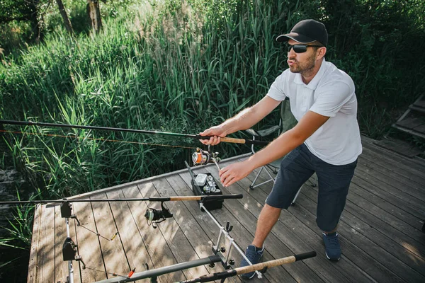 湖や川で若い漁師釣り。漁業の様子。手に2本の棒と釣りを持ってる。桟橋に一人で立つ. — ストック写真