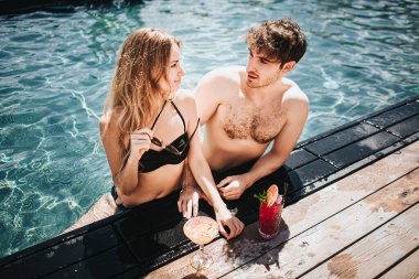 Genç ve seksi bir çift yüzme havuzunda dinleniyor. Mayolu seksi erkek ve kadın birbirlerine bakıyorlar. Yüzme havuzunda durup poz vermek. Lezzetli kokteyller ve lüks spa merkezleri.