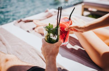 Genç ve seksi bir çift yüzme havuzunda dinleniyor. Kokteyl tutan kadın ve erkeklerin el resimleri. Buzlu, buzlu bir içecek. Yaz tatilinde yüzme havuzunda iyi eğlenceler. Resort spa yeri.