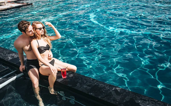 Joven pareja caliente descansando en la piscina. Sexy hombre y mujer hermosa pasar tiempo de vacaciones juntos arte agua. El tipo se sienta detrás de la chica disfrutando de su compañía. Tiempo de spa Resort . — Foto de Stock