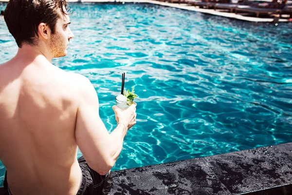Joven hombre caliente descansando en la piscina. Recorta la vista de un tipo fuerte y poderoso sosteniendo un cóctel en la mano y disfruta pasar tiempo en el agua. Vacaciones de verano . — Foto de Stock