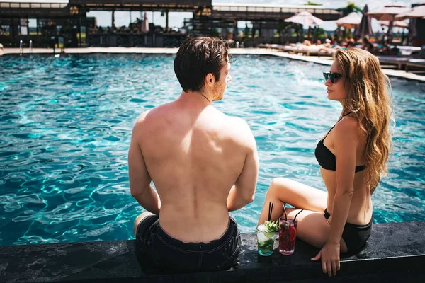 Joven pareja caliente descansando en la piscina. Precioso sexy hombre y mujer mirarse el uno al otro. Pase tiempo en el agua en el spa del complejo. Vacaciones de verano en el hotel. Día soleado brillante . — Foto de Stock