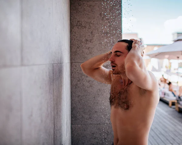 Joven duchándose afuera. Topless fuerte tipo poderoso lavando la cabeza y el cuerpo. Disfrutando del proceso de caída del agua. Descanse las vacaciones de verano en el balneario . — Foto de Stock
