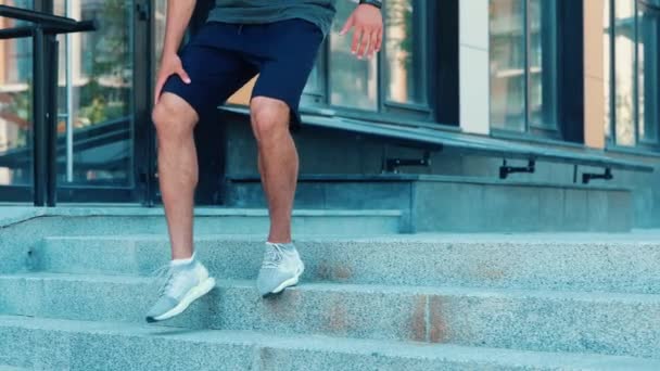 Jovem se exercitando lá fora. Movimento lento de desportista cansado exausto derramando água sobre si mesmo após o treinamento ou treino. Fique na rua e segure a garrafa com água limpa . — Vídeo de Stock