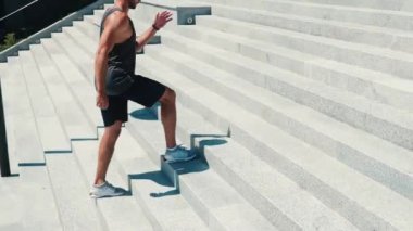 Genç adam dışarıda egzersiz yapıyor. Hareketsiz duran güçlü adam bir adım atlıyor. Beyaz kulaklıkla müzik dinle. Dışarıda tek başına çalışmanın tadını çıkar. Güneşli güzel bir gün.