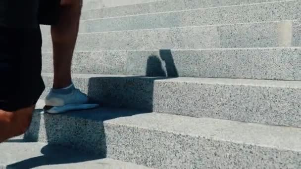 Jovem se exercitando lá fora. Visão lateral traseira de pernas caras fazendo exercícios de agachamento de uma perna dando um passo à frente e pulando um passo. Exercício na rua sob o sol . — Vídeo de Stock