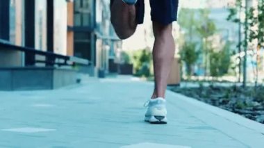 Genç adam dışarıda egzersiz yapıyor. Arka planda güçlü, zayıf ve formda erkek bacaklarının koşuşunu ve sokak boyunca koşan ışığın kentsel binaların önünden geçişini gösteren bir video var. Dışarıda egzersiz yapıyorum..