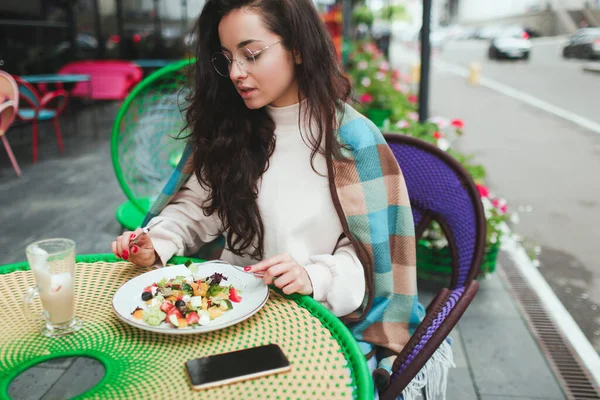 Genç kadın kafe veya restoranda yalnız oturuyor. Öğle yemeği saatinde dışarıda salata yiyen ciddi meşgul bir kız. Tek başına oturup, onun yanında akıllı telefon tutmak.. — Stok fotoğraf