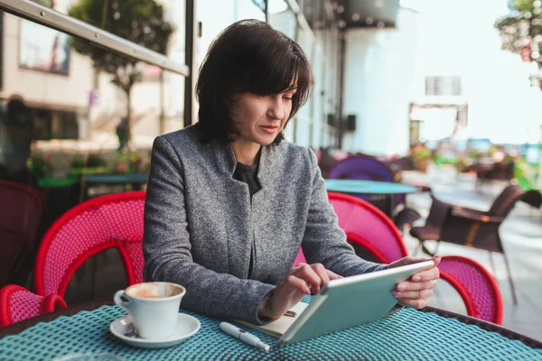 Mulher de negócios madura sentar-se sozinho e pensar. Trabalhando sozinho usando tablet moderno. A escrever no ecrã. Além disso, uma chávena de chá ou café. Trabalhando em novo plano de negócios ou projeto. — Fotografia de Stock