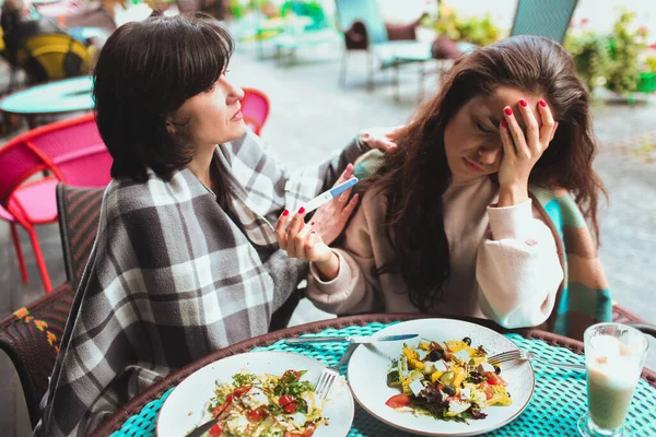 Mère mature et sa jeune fille s'assoient ensemble dans un café ou un restaurant. Fille inquiète bouleversée montrant test de grossesse positif à sa mère. Femme mûre essayer de se calmer fille adulte. Réaction dure. — Photo