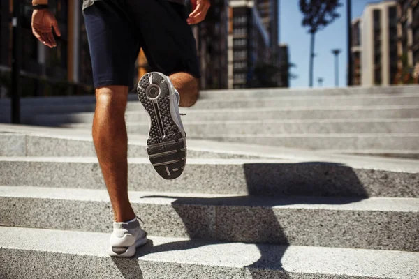 Young man exercising outside. Back low view of strong males legs, calfs and feet in sneakers. Athletist jogging or unning up steps. Training and having workout outside. Shadow from body.