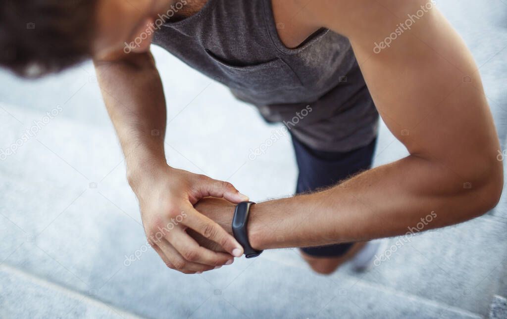 Young man exercising outside. Up view of strong powerful guy checking his result on fitness tracker on his hand. Time tracking. Walking on steps.