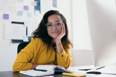 Kendinden emin ve başarılı bir lider. Sarı elbiseli, kendine güvenen genç bir kadın eline dayanıp gülümseyerek kameraya bakıyordu. Siyah masada açık planlayıcı. Evde ya da ofiste çalışmak.