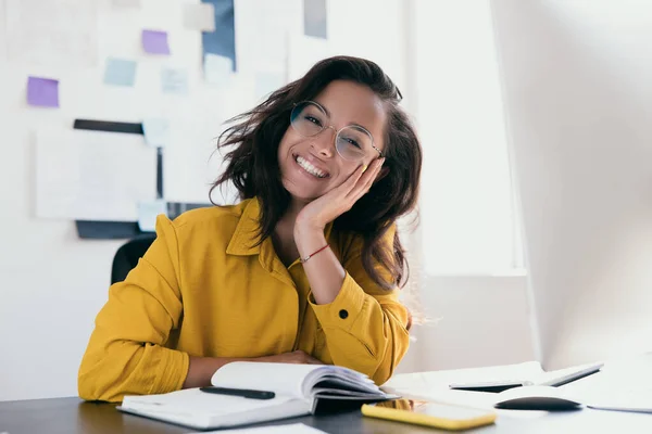 Freelancer feminino confiante e bem sucedido. Jovem confiante apoiou seu queixo na palma da mão olhando para a câmera com sorriso. Freelancer feliz ou trabalhador de escritório. Menina de aparência profissional em camisa amarela — Fotografia de Stock