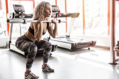 Bir kadın spor salonunda halterle ağırlık kaldırıyor..