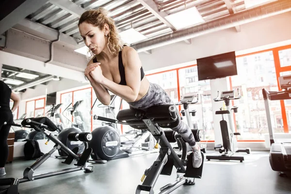 Una donna è sdraiata su un attrezzo da addestramento. Sta allenando i muscoli addominali. — Foto Stock