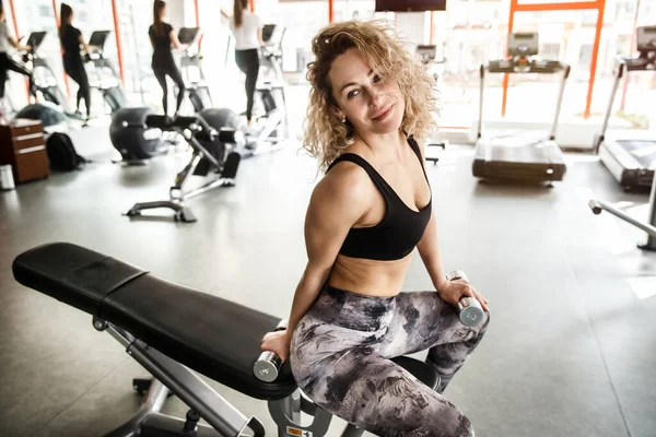 Uma mulher está sentada num aparelho de treino. Ela está olhando para longe e sorrindo — Fotografia de Stock