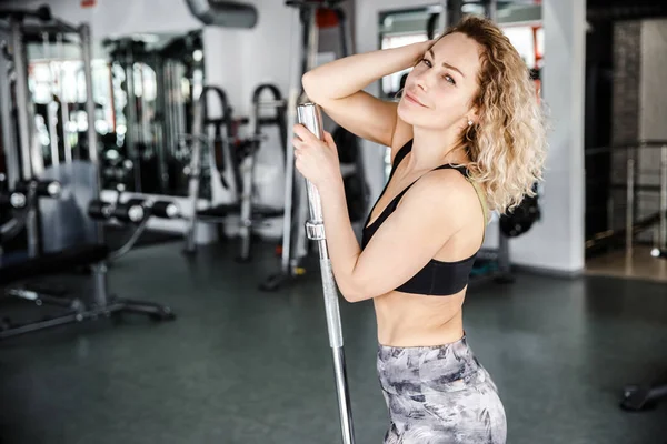 Uma mulher está num ginásio brilhante. A mão dela está numa campainha. Ela está olhando para a câmera e sorrindo — Fotografia de Stock