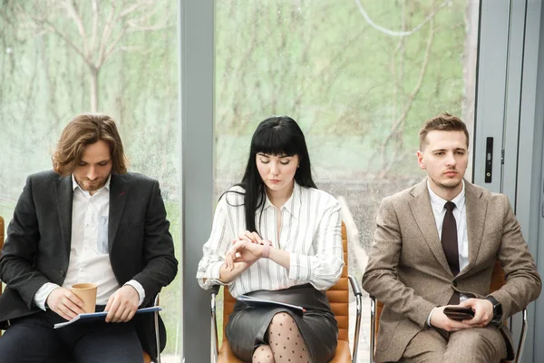 Три офисных работника ждут встречи. Женщина посередине смотрит на часы — стоковое фото
