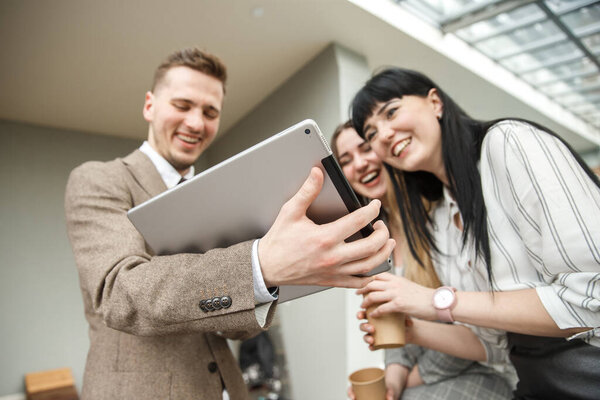 A guy is showing something on his big tablet to a two laughing girls
