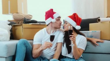 Genç çift yeni bir daireye taşınıyor. 2021 yılbaşı. Yeni dairede Noel 'i kutlayan bir çift. Birlikte yere oturun ve kırmızı şarap için. Birbirinize eşlik edin..
