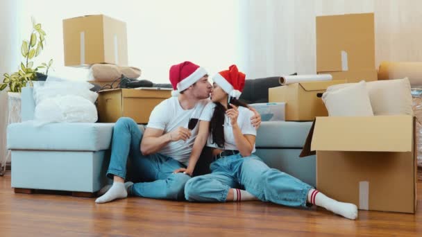 Una pareja joven se muda a un apartamento nuevo. Período de año nuevo o Navidad. Pareja sentarse en el suelo y celebrar las vacaciones en un apartamento nuevo. Beber vino y divertirse. — Vídeo de stock