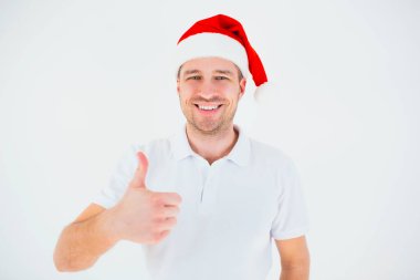 Genç adam beyaz arka planda izole edilmiş. Şenlikli Noel şapkalı adam başparmağını kaldırdı ve gülümsedi. Kamerada poz veren neşeli, pozitif, hoş bir adam. Noel zamanı ya da yeni yıl aralığı.