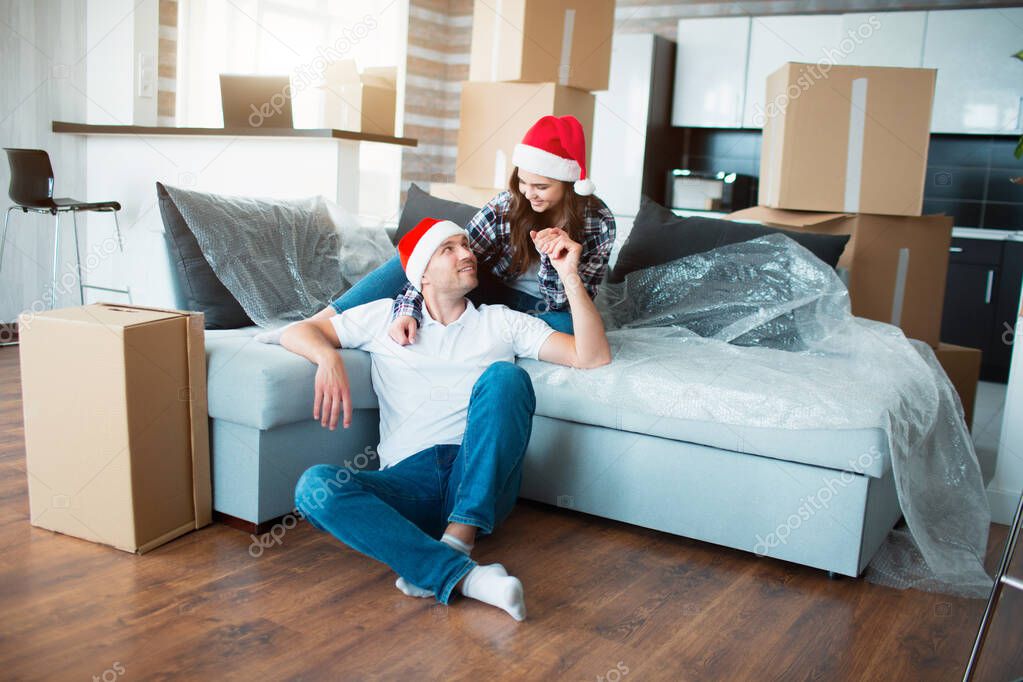 Newlywed couple celebrate Christmas or New Year in their new apartment. Young happy man and woman celebrating moving to new home and sitting among boxes.