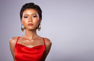 Fashion Young bronzlaşmış tenli, zayıf Asyalı kadının portresi kısa saçlı, kırmızı cüppeli, güçlü duruşlar sergiliyor. Stüdyo gri Arkaplan kopyalama alanı