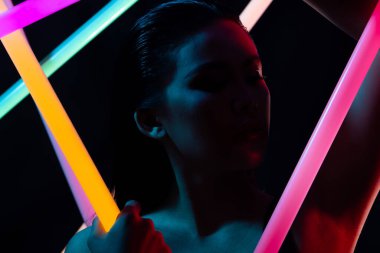 Yüksek Moda Trend Kozmetik Makyajı 'nın Yüzü NEON tüpü ışığı ile kapanıyor, düşük pozlu genç Asyalı kadının tenine etki ediyor, LED çizgisi renginde duygularını ifade ediyor, uzay siyah arka planlarını kopyalıyor