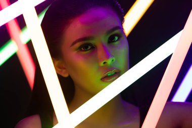 Yüksek Moda Trend Kozmetik Makyajı 'nın Yüzü NEON tüpü ışığı ile kapanıyor, düşük pozlu genç Asyalı kadının tenine etki ediyor, LED çizgisi renginde duygularını ifade ediyor, uzay siyah arka planlarını kopyalıyor