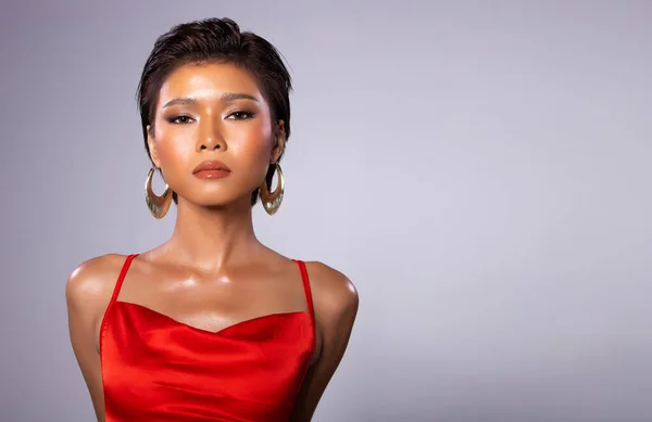 Fashion Young bronzlaşmış tenli, zayıf Asyalı kadının portresi kısa saçlı, kırmızı cüppeli, güçlü duruşlar sergiliyor. Stüdyo gri Arkaplan kopyalama alanı