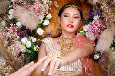 Hint güzeli yüzü mükemmel makyaj gelini, kırmızı pembeli güzel bir kadının portresi geleneksel Hindistan gelinliği, ağır mücevherler ve el ele tutuşmalar, bakış açısı.