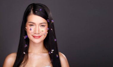 20 'li yaşlarda, Asyalı bir kadının yarı vücut portresi. Siyah saçlı, beyaz elbise. Kız, çiçek pedalını saçlarına takar ve gülümser. Gri arka planda pek çok poz verir.