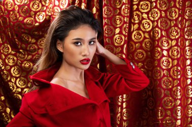 Moda 20 'li yaşlardaki Asyalı kadının portresi fırça ve renk rujunda güzel bir makyaj sanatçısına sahip, kırmızı altın arka plan fotokopi alanının üzerine kırmızı ceket giyiyor.