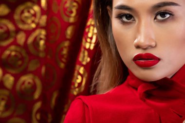 Moda 20 'li yaşlardaki Asyalı kadının portresi fırça ve renk rujunda güzel bir makyaj sanatçısına sahip, kırmızı altın arka plan fotokopi alanının üzerine kırmızı ceket giyiyor.