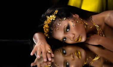 Moda 20 'li yaşlardaki Asyalı kadının portresi fırçasında güzel bir makyaj sanatçısı, yüzünde şık bir altın yaprak ile süslüyor ve aynayı yansıtıyor, boşluğu kopyalıyor.