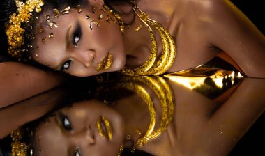 Moda 20 'li yaşlardaki Asyalı kadının portresi fırçasında güzel bir makyaj sanatçısı, yüzünde şık bir altın yaprak ile süslüyor ve aynayı yansıtıyor, boşluğu kopyalıyor.