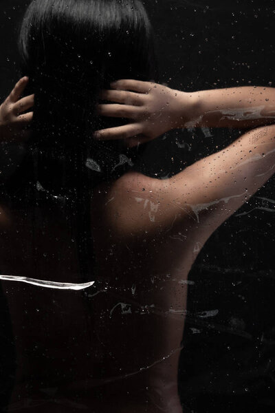 Turn back side Sexy art nude female. Naked sensual black hair Asian woman erotic poses with feeling arouse light shadow and silhouette in bathroom shower glass steam over dark background copy space